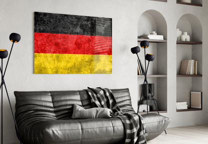 German flag glass wall art with black, red, and yellow horizontal stripes displayed above a black leather sofa in a modern living room.