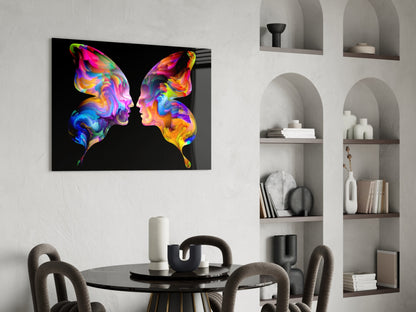 Colorful glass wall art featuring two vibrant butterfly silhouettes facing each other against black background, displayed above round black table in modern room setting.