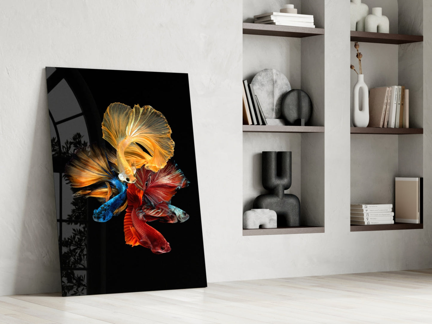 Glass wall art leaning against white wall displays three colorful betta fish in gold, blue, and red against black background.