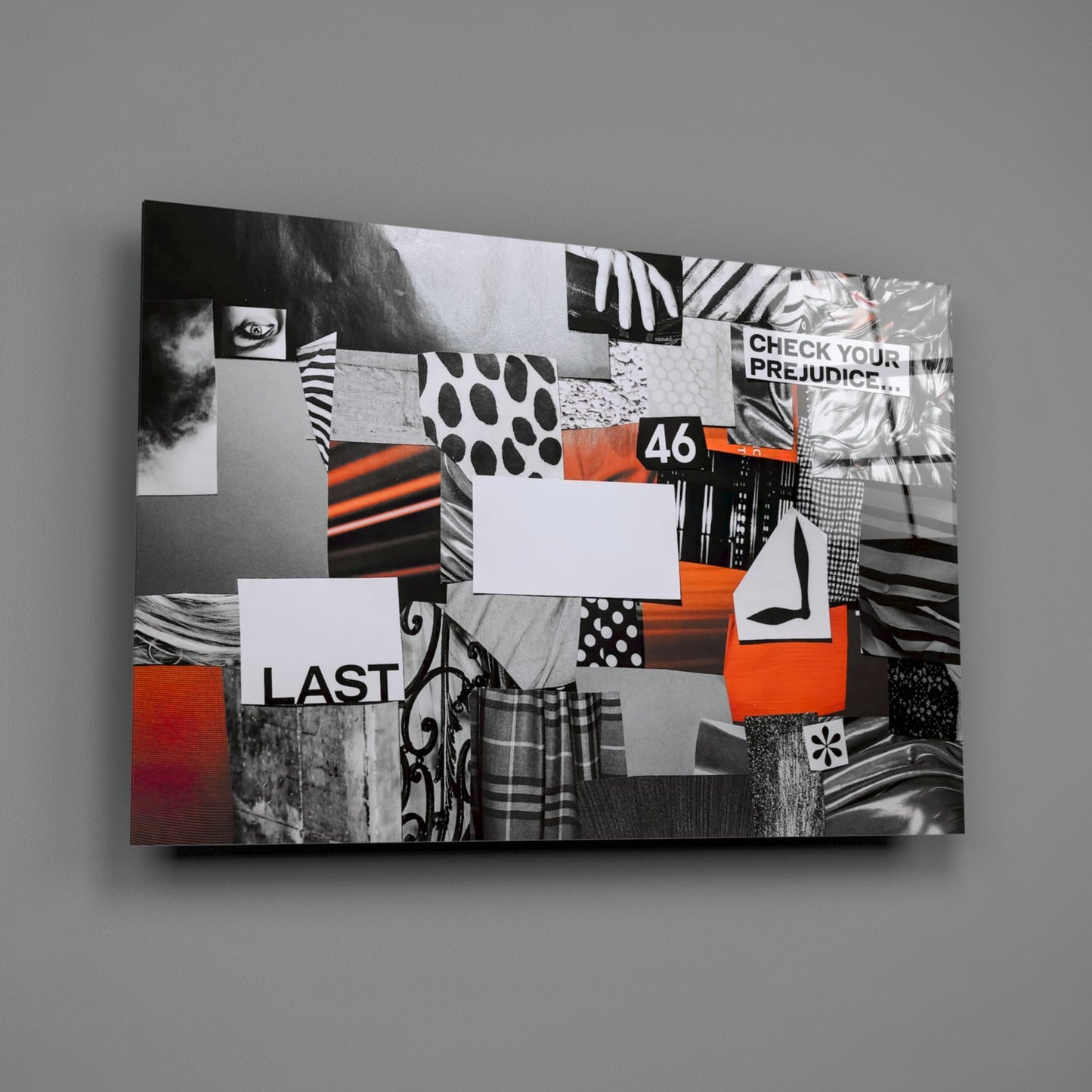 Angled view of glass wall art featuring black-and-white patterned collage with orange accents, displaying "CHECK YOUR PREJUDICE," "46," and "LAST" text.
