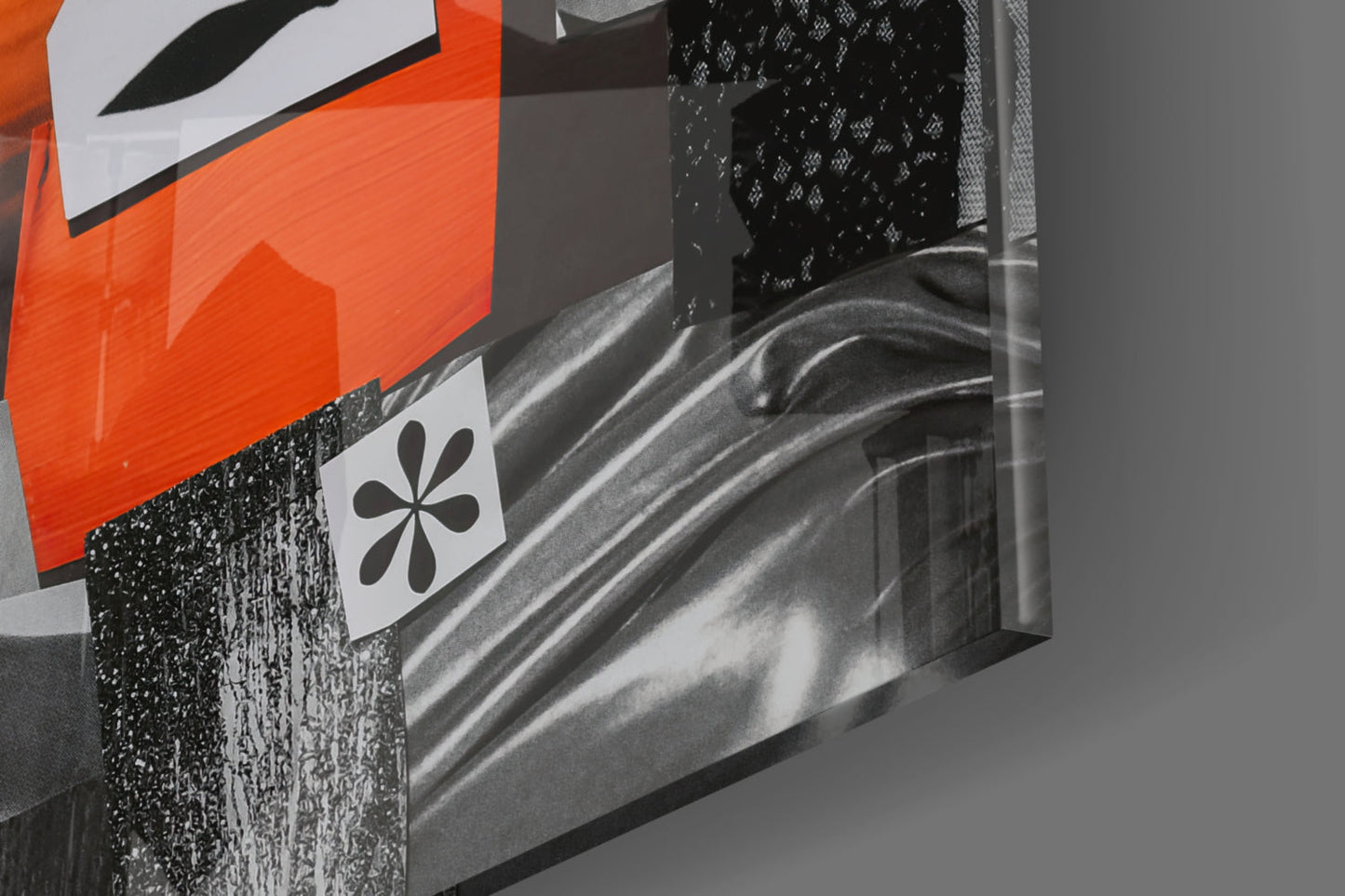 Close-up angled view of glass wall art with orange geometric shapes, black flower symbol, and textured black surface detail.