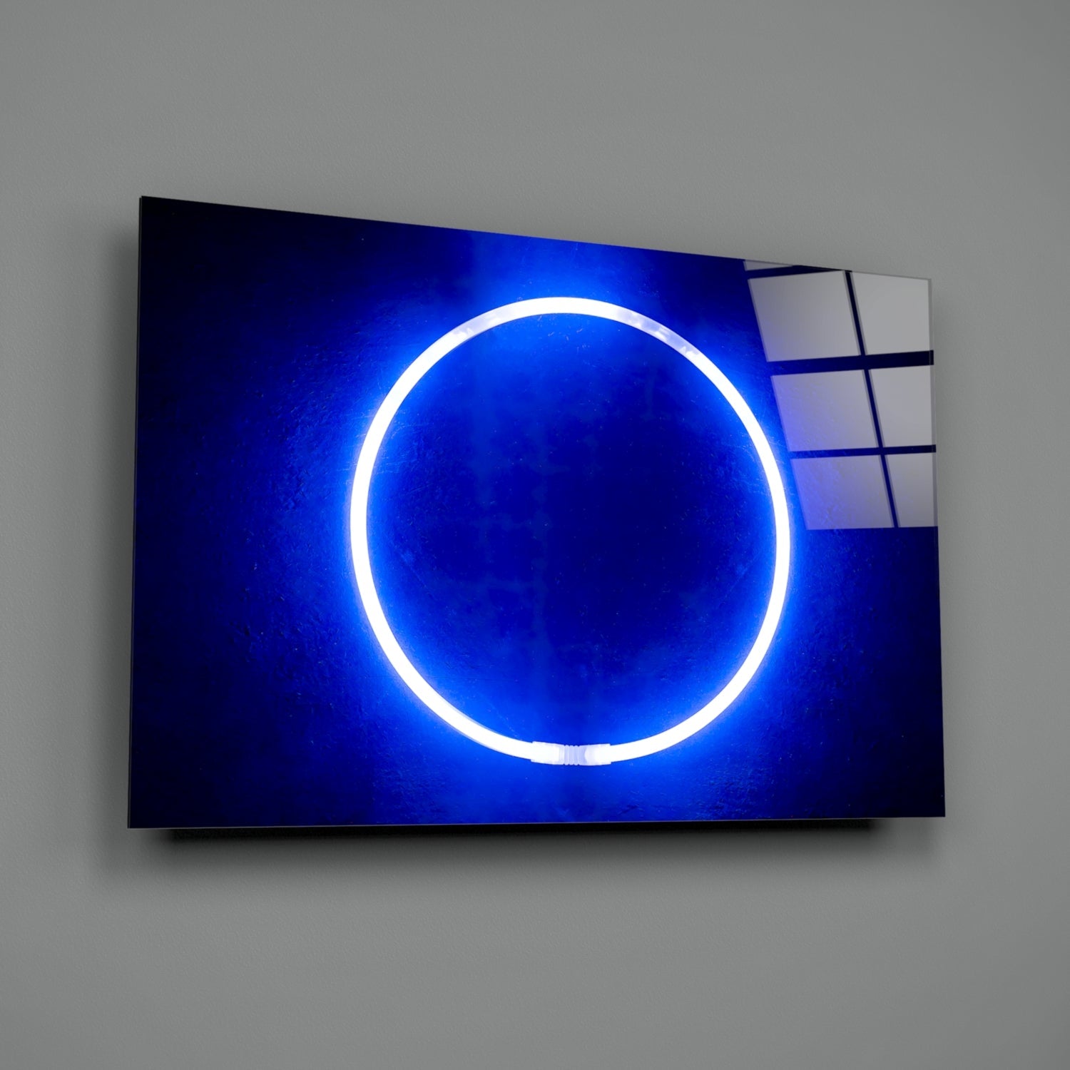 Illuminated blue neon circle on dark glass panel mounted on gray wall, angled three-quarter view.