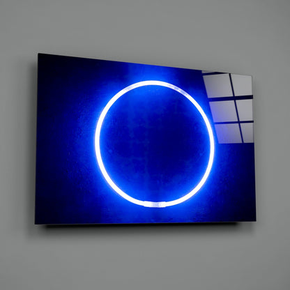 Illuminated blue neon circle on dark glass panel mounted on gray wall, angled three-quarter view.