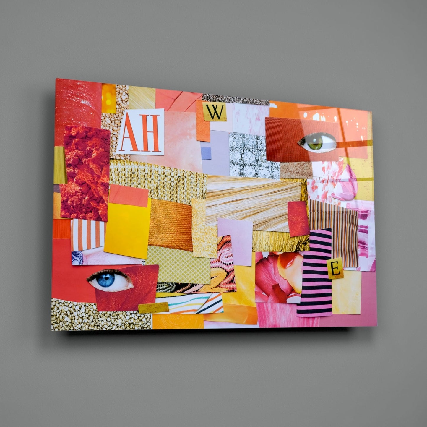 Colorful modern patchwork glass wall art with red, yellow, pink, and orange fabric squares, eyes, and letters "AH," "W," and "E" displayed at an angle against gray background.