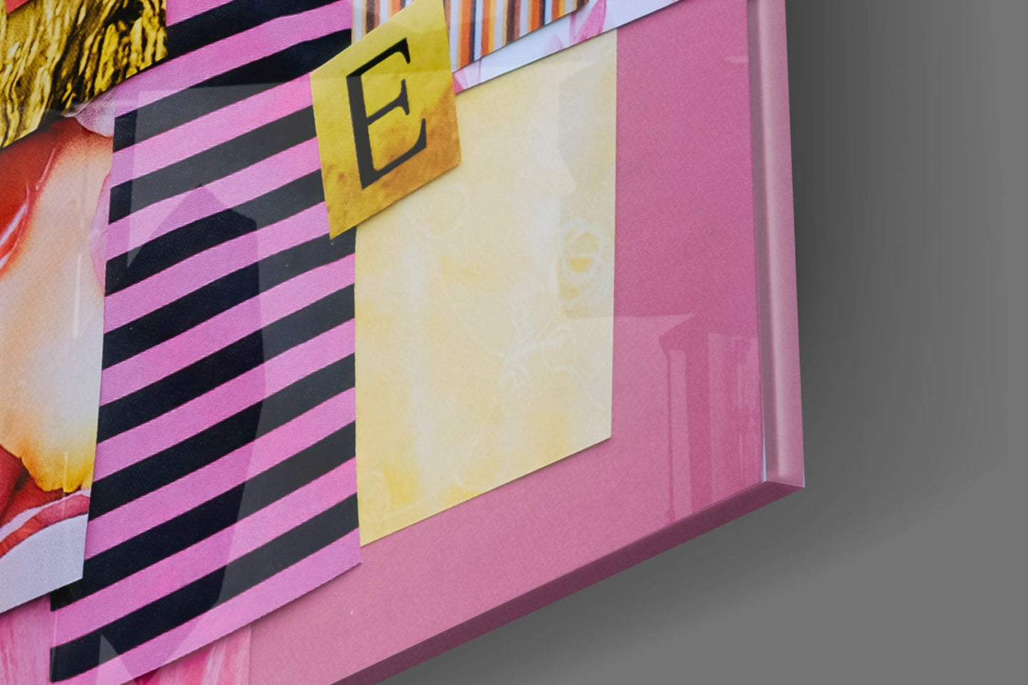 Close-up detail of pink glass wall art with black horizontal stripes, yellow letter "E," and cream-colored section.