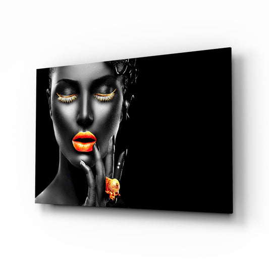 Black and white portrait of a woman with gold eyelashes and orange lips and jewelry, displayed on a glass wall art panel.