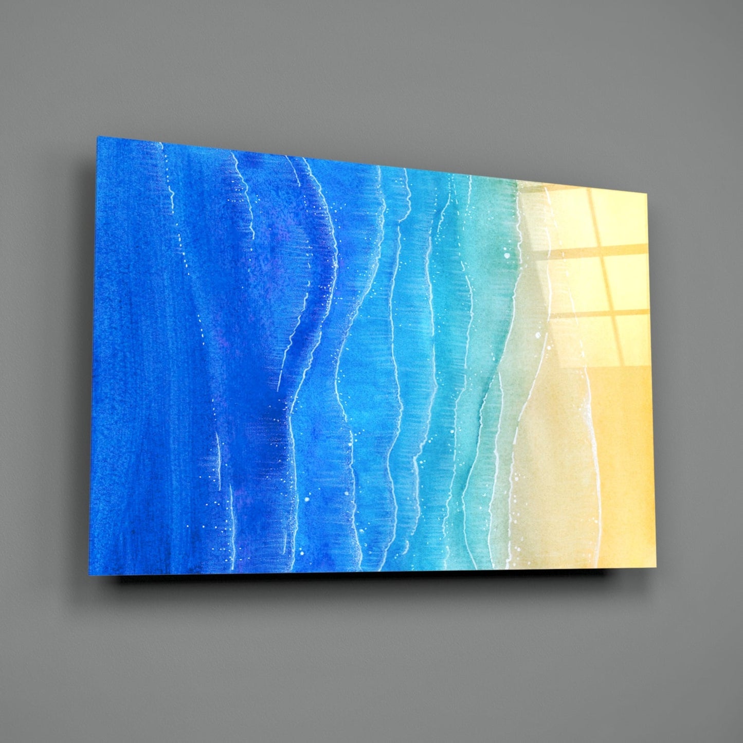 Angled view of glass wall art depicting ocean waves transitioning from deep blue to turquoise to pale yellow sand.