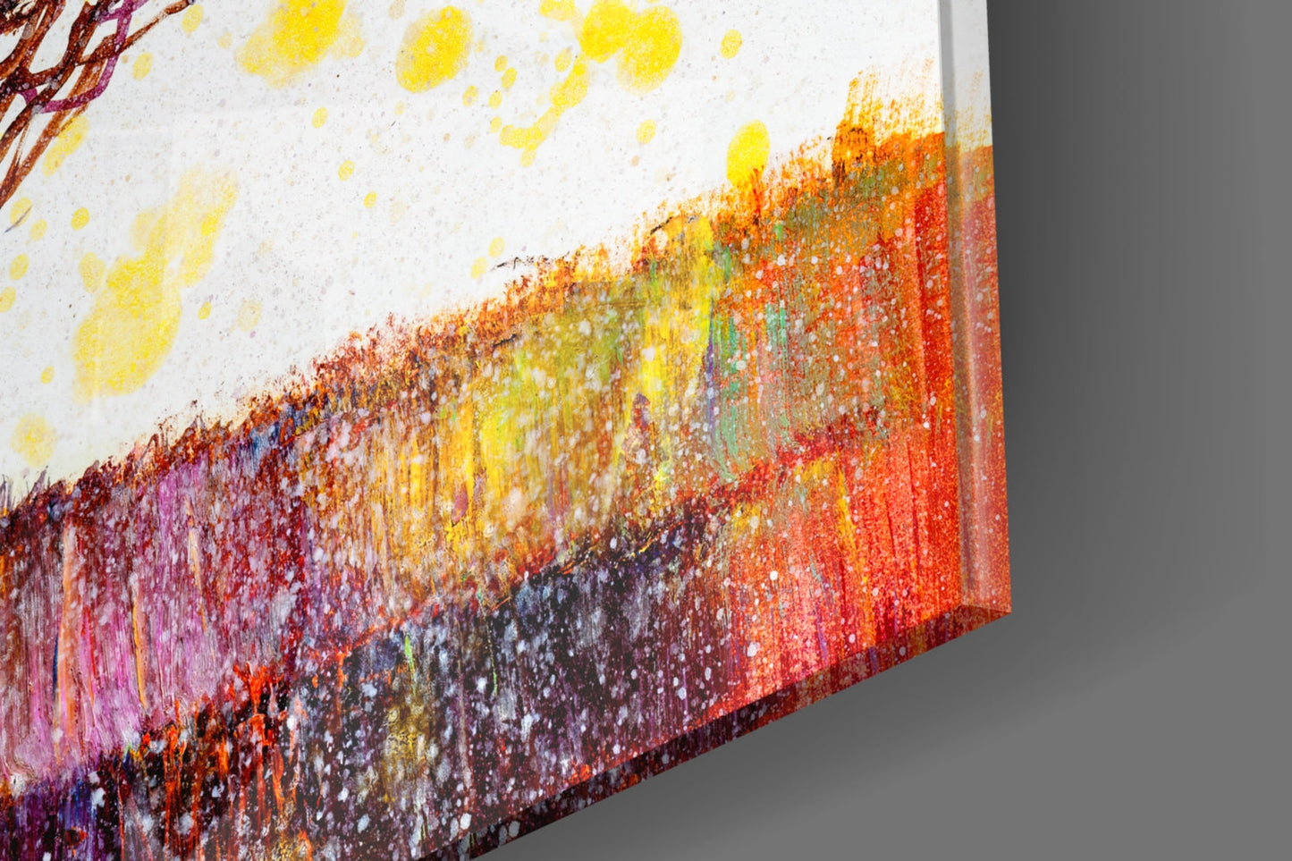 Close-up angled view of colorful tree glass wall art showing vibrant yellow, orange, red, and purple brushstroke transitions with textured surface detail.