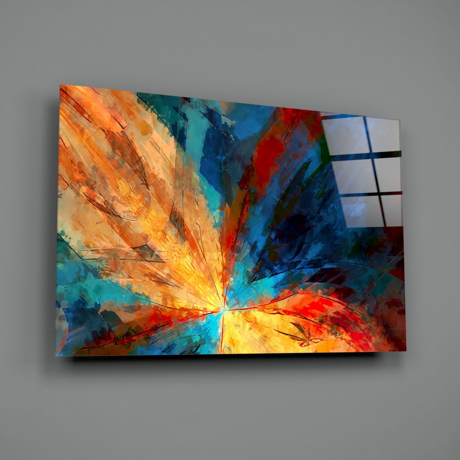 Colorful glass wall art displaying a radiant fractal flower design with orange, yellow, blue, and red rays emanating from center, mounted on gray wall.
