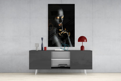 Portrait glass wall art depicting a dark-skinned woman with gold accents displayed above a gray media console in a minimalist interior setting.