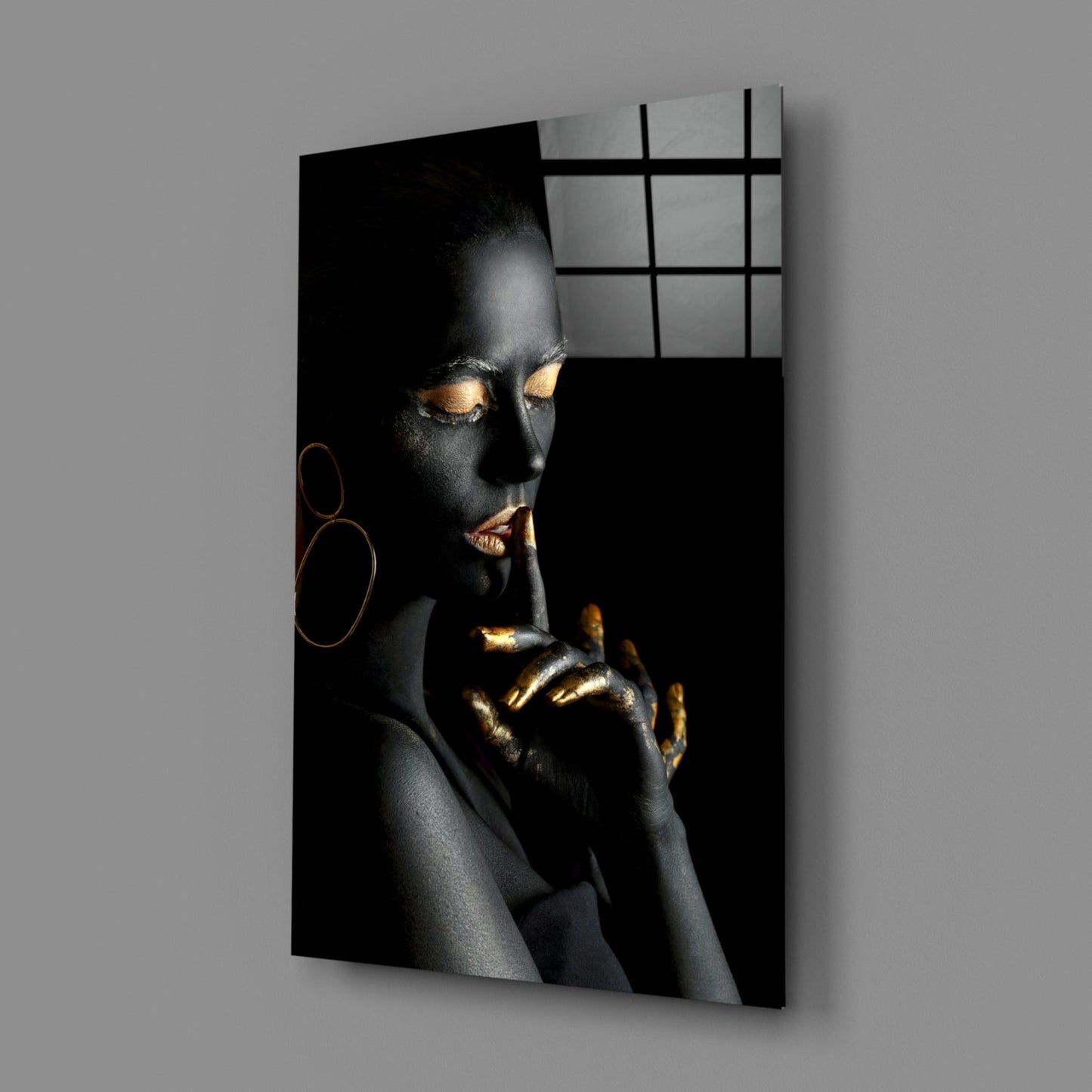 Glass wall art displaying a woman with black skin and gold accents, shown at an angle against a gray wall.