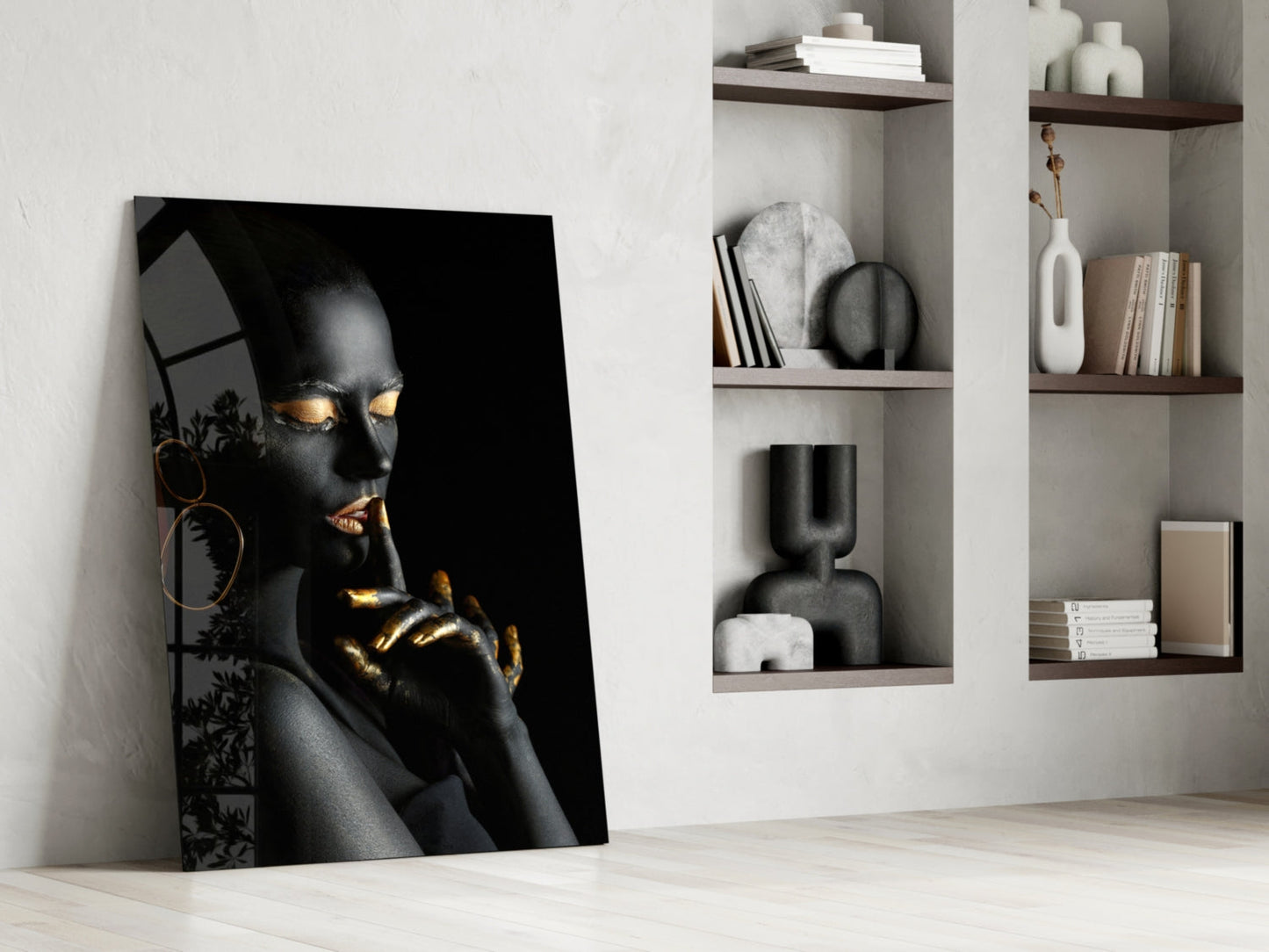 Black and gold portrait glass art leaning against white wall beside wooden shelving with decorative objects and books.