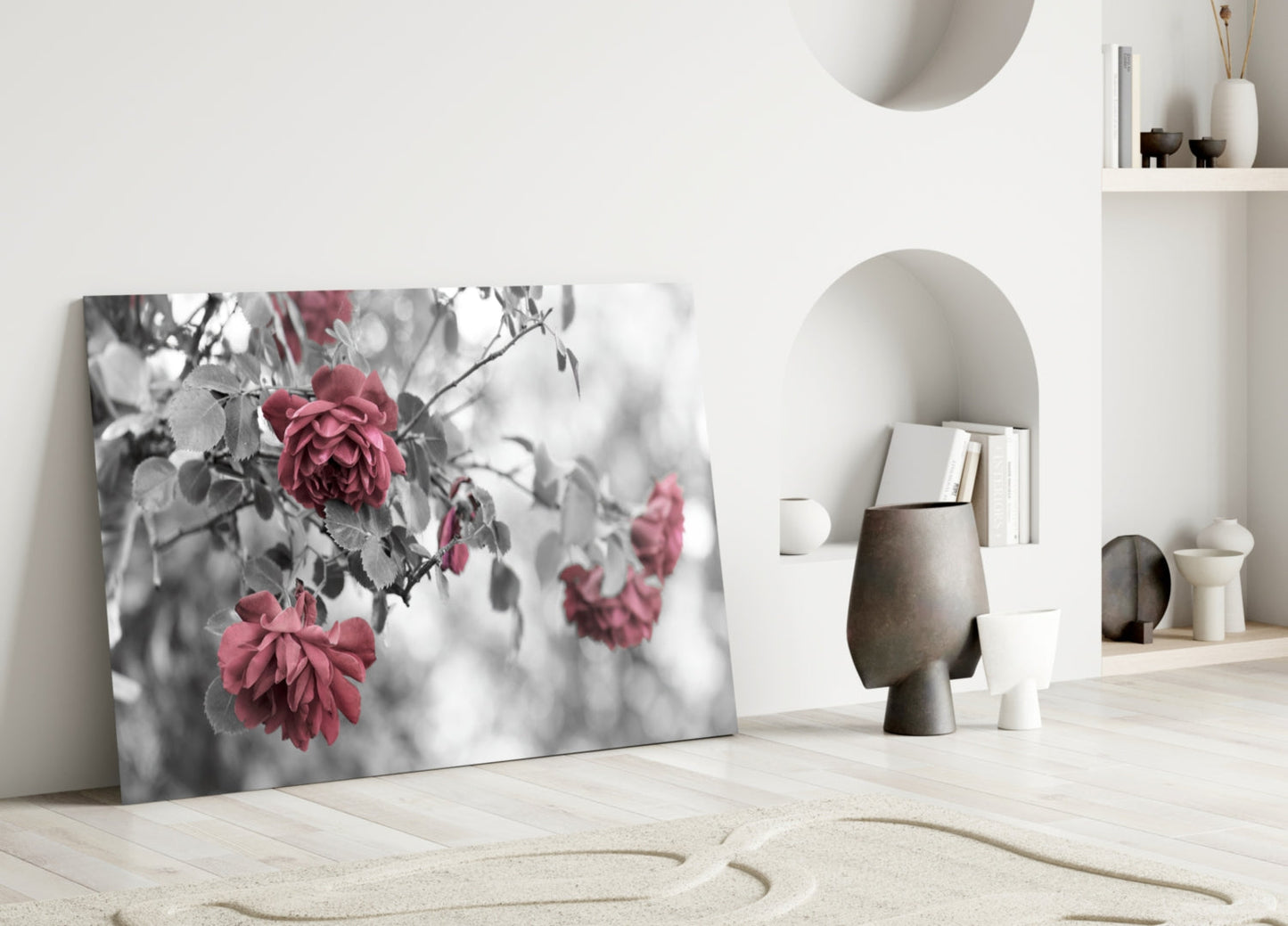 Glass wall art leaning against white wall displaying black and white roses with selective pink color in minimalist interior setting.