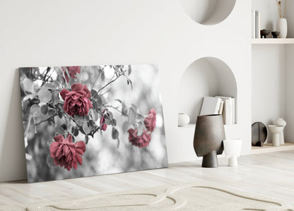 Glass wall art leaning against white wall displaying black and white roses with selective pink color in minimalist interior setting.