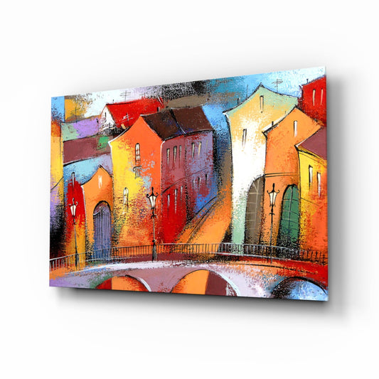Vibrant glass wall art depicting colorful stone buildings with a bridge, displayed at an angle against white background.