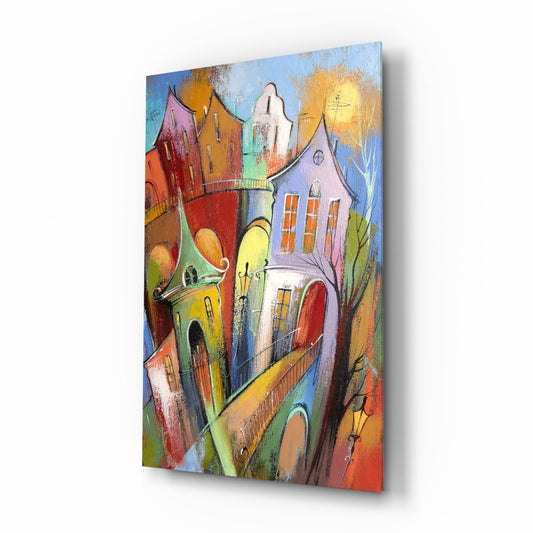Angled view of colorful glass wall art featuring whimsical tilted houses with vibrant reds, yellows, blues, and greens under a golden sun.