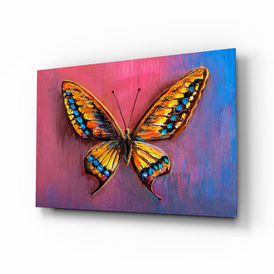 Vibrant amber and gold butterfly with blue spot markings centered on gradient pink-to-blue painted glass panel, angled three-quarter view.