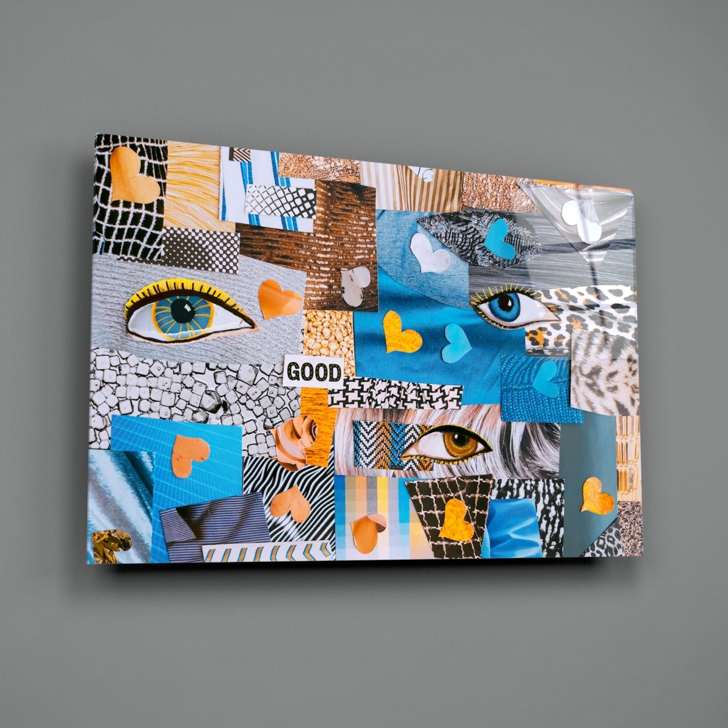 Abstract Confusion Glass Wall Art displayed at an angle, revealing colorful patchwork squares with eyes, hearts, patterns, and "GOOD" text in blue, orange, and neutral tones.