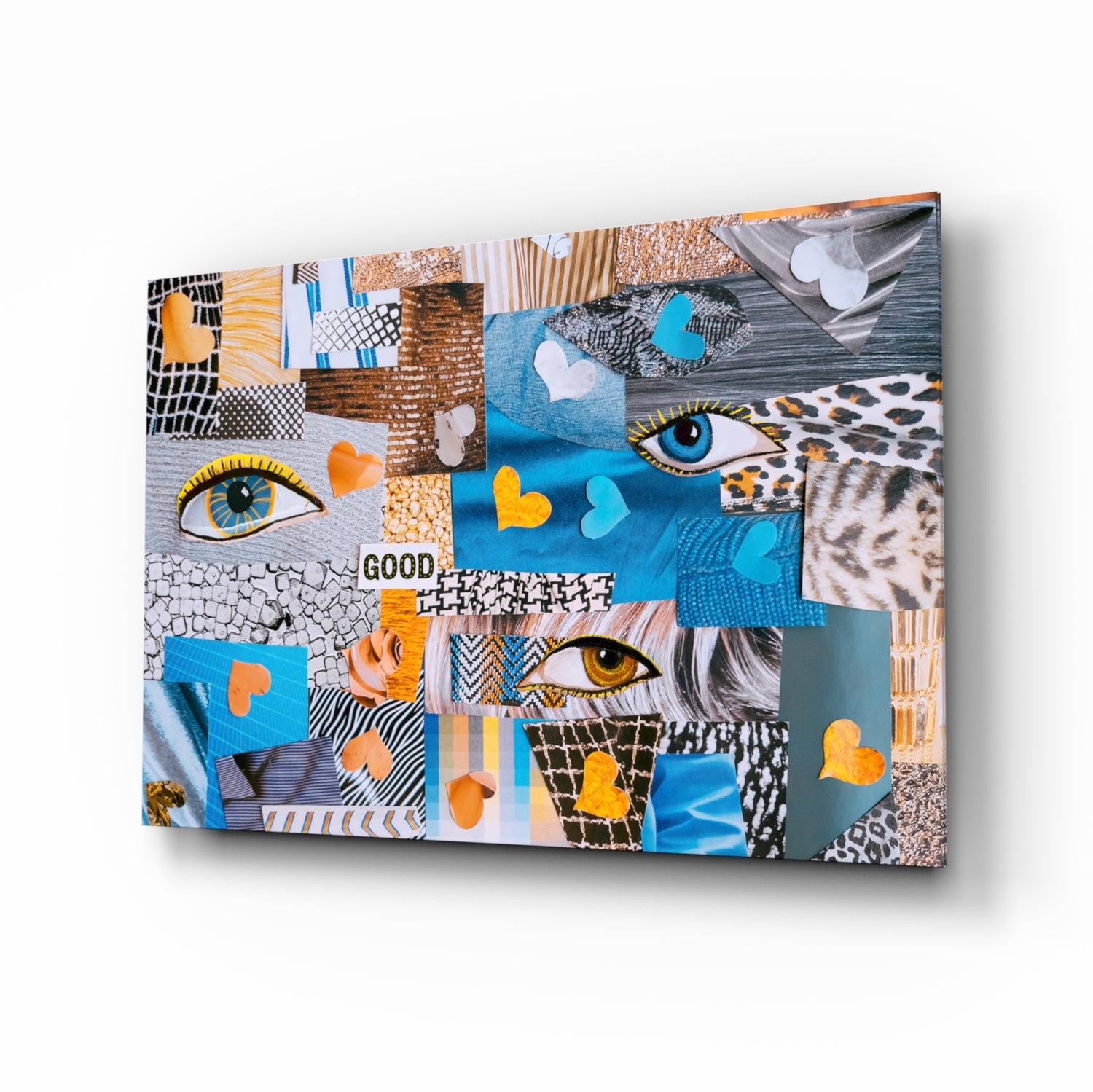 Abstract Confusion Glass Wall Art displayed at an angled perspective showing colorful patchwork design with eyes, hearts, patterns, and "GOOD" text in blue, orange, and neutral tones.