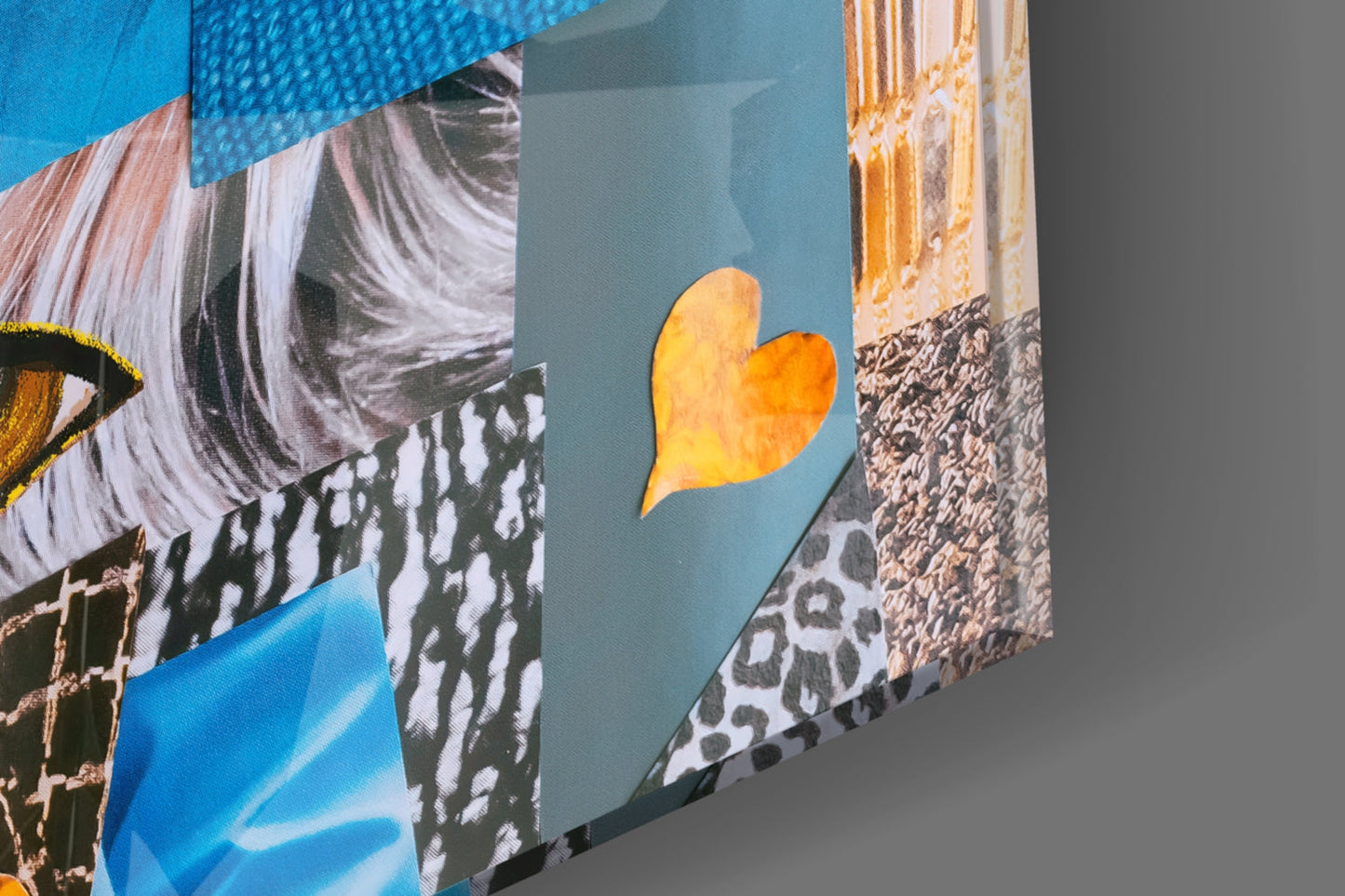 Close-up angled view of glass wall art panels showing blue background, golden heart shape, textured patterns, and architectural imagery in multiple overlapping sections.