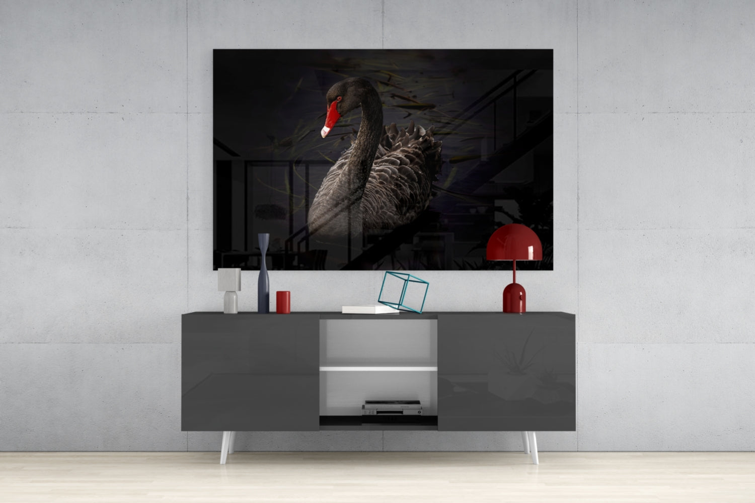 Black swan glass wall art mounted above gray media console with red lamp and decorative accessories in modern living room setting.