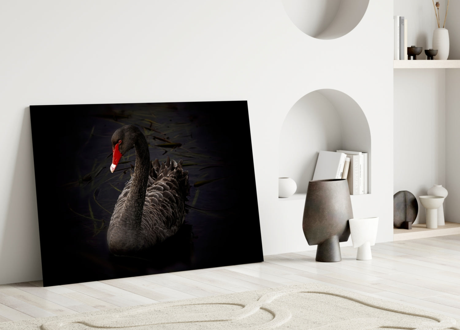 Black swan glass wall art leaning against white wall in minimalist interior with decorative objects and shelving.