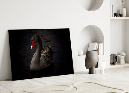 Black swan glass wall art leaning against white wall in minimalist interior with decorative objects and shelving.