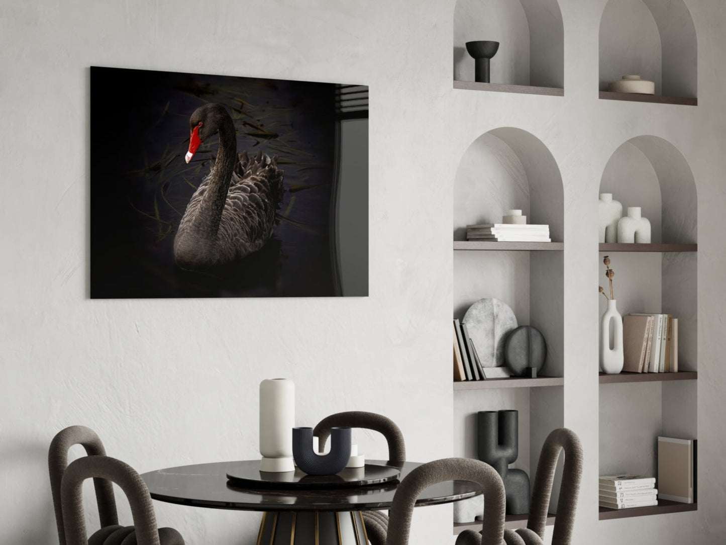 Black swan glass wall art with red beak displayed above dining table in modern interior setting.