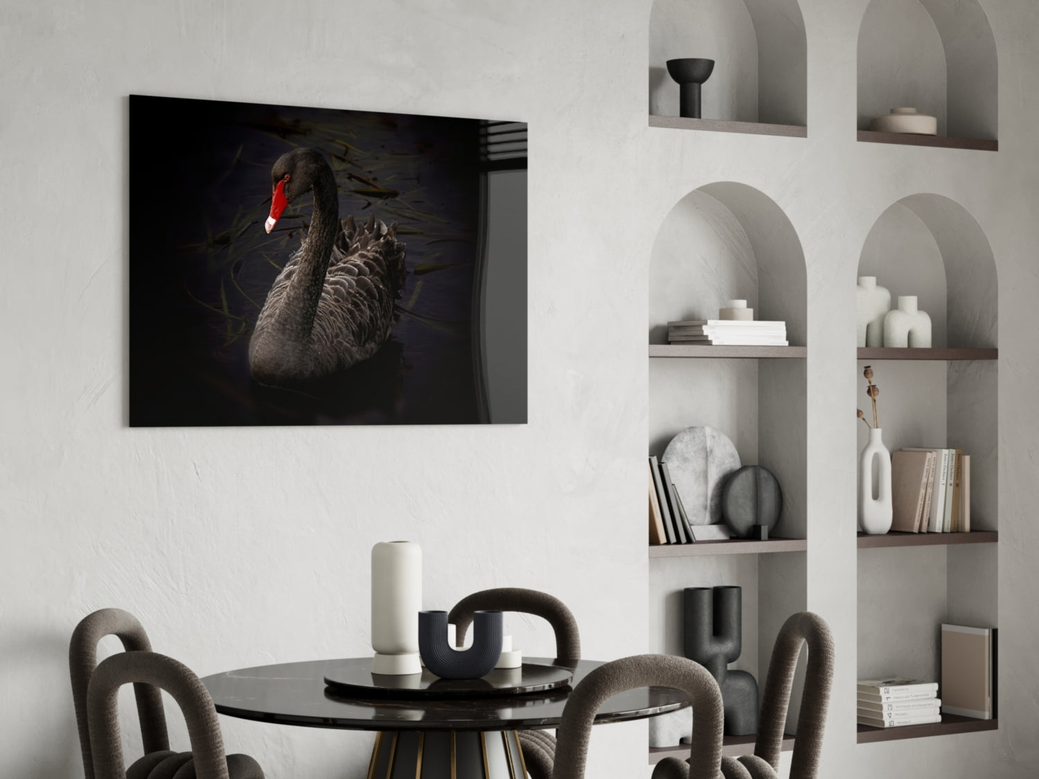 Black swan glass wall art with red beak displayed above dining table in modern interior setting.