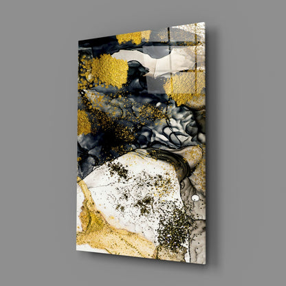 Angled view of glass wall art displaying gold leaf, black ink, white, and grey abstract swirls mounted on gray background.