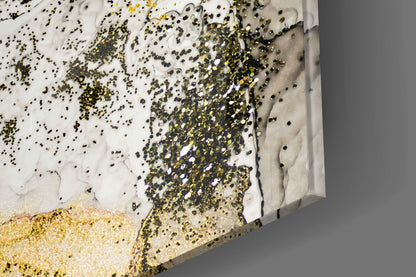 Close-up angled view of glass wall art with white resin base, gold and black glitter scattered across surface, and sandy gold texture at bottom edge.
