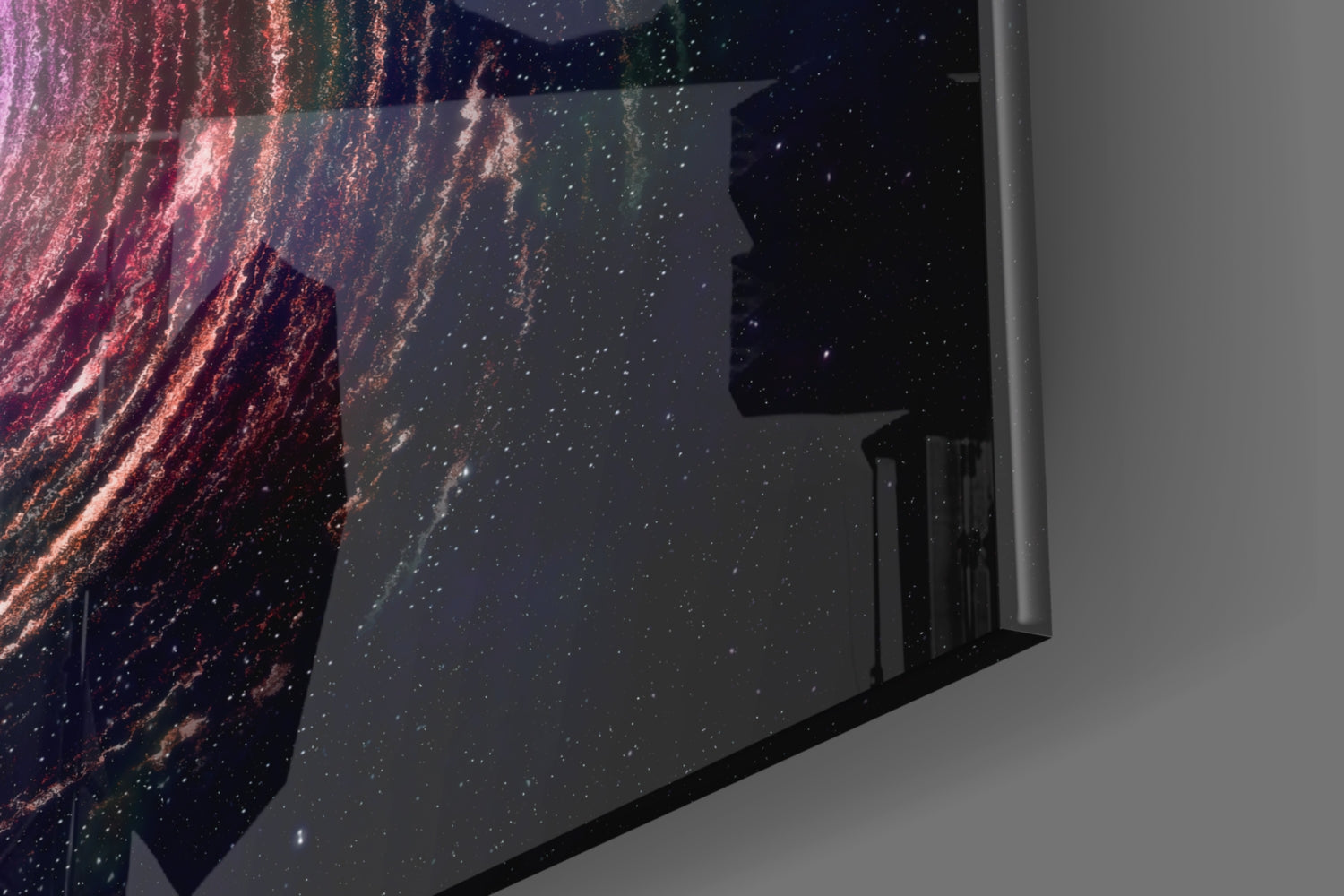 Angled view of glass wall art displaying a spiral galaxy with pink, red, and green nebula against black starfield, mounted on white wall.
