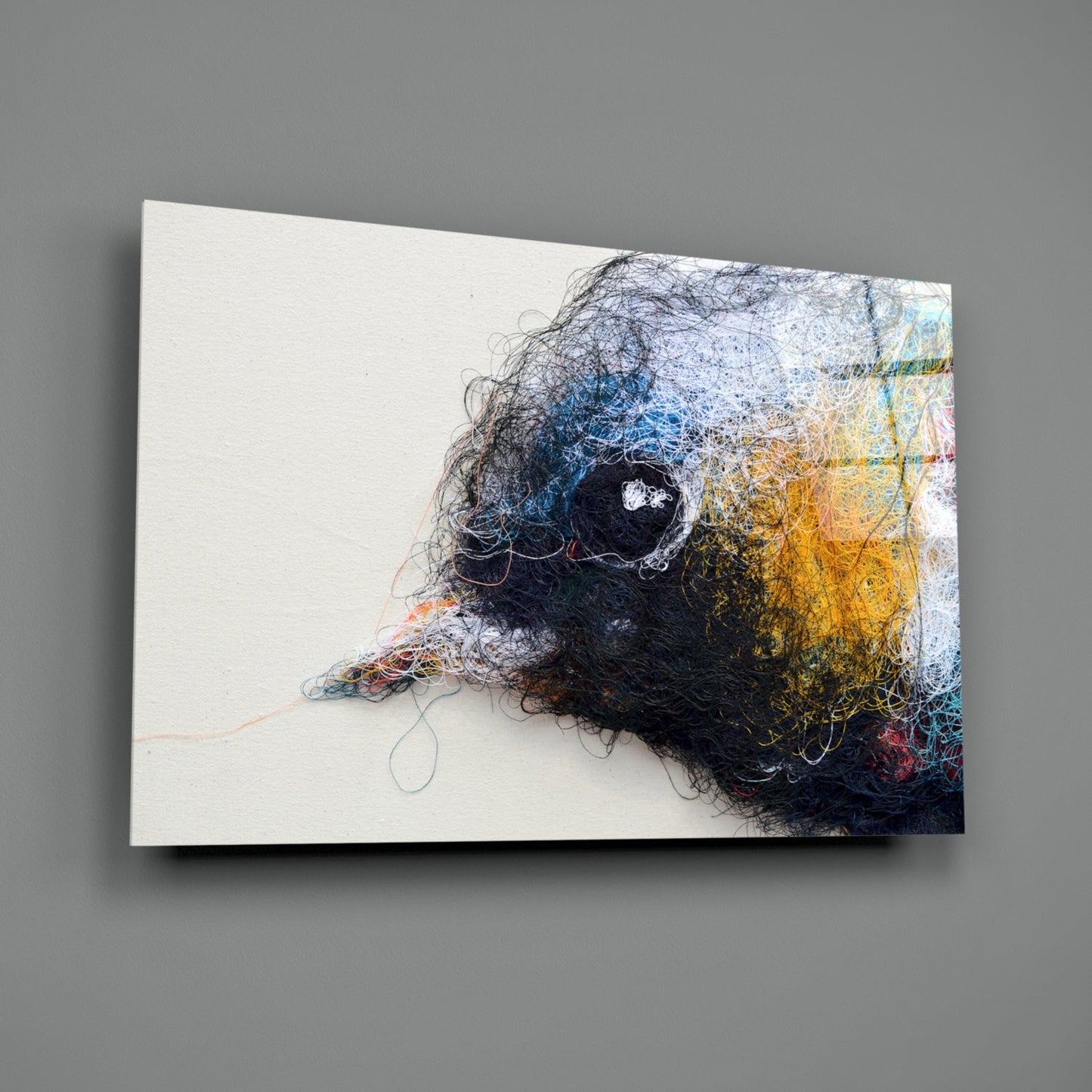 Three-dimensional glass wall art featuring an abstract bird head profile with tangled black, blue, yellow, and white thread-like strands on cream background, mounted at angle.