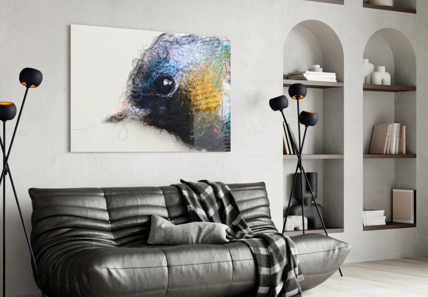 Abstract bird head wall art in blue, yellow, and black thread on white canvas, displayed above black leather sofa in modern living room.