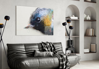 Abstract bird head wall art in blue, yellow, and black thread on white canvas, displayed above black leather sofa in modern living room.