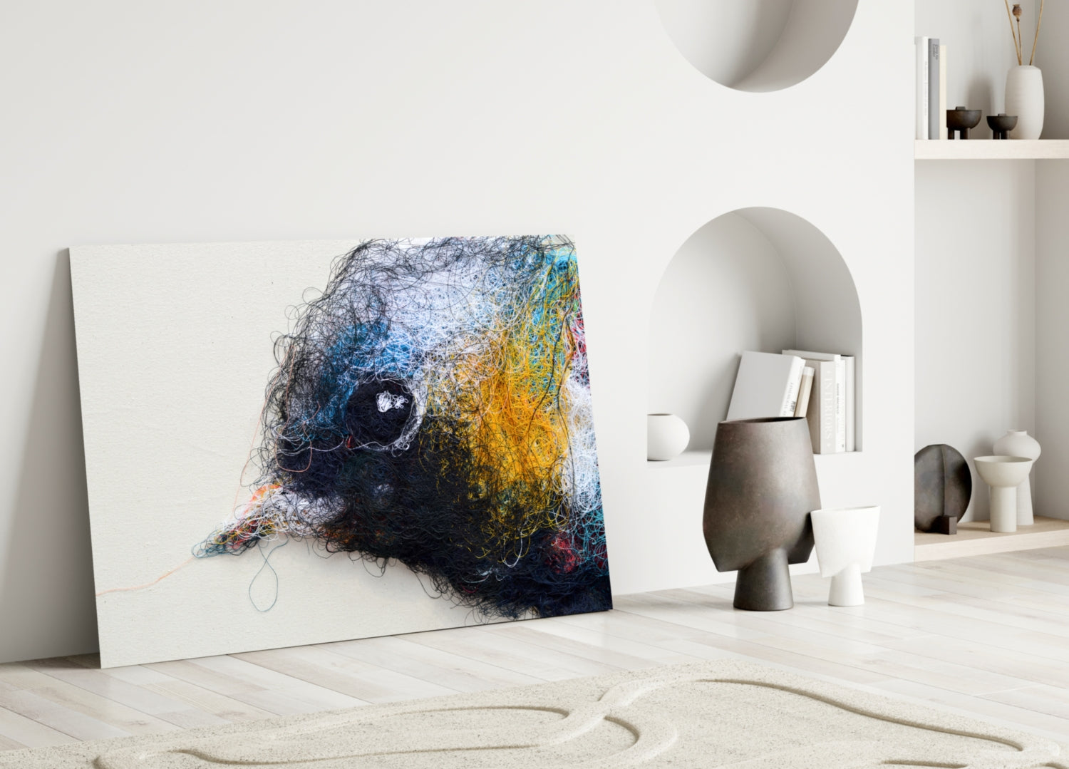 Abstract glass wall art featuring tangled navy, blue, and golden yellow threads with a dark circular center, leaning against white wall in minimalist interior.