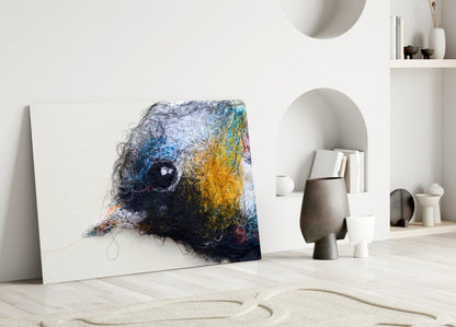 Abstract glass wall art featuring tangled navy, blue, and golden yellow threads with a dark circular center, leaning against white wall in minimalist interior.