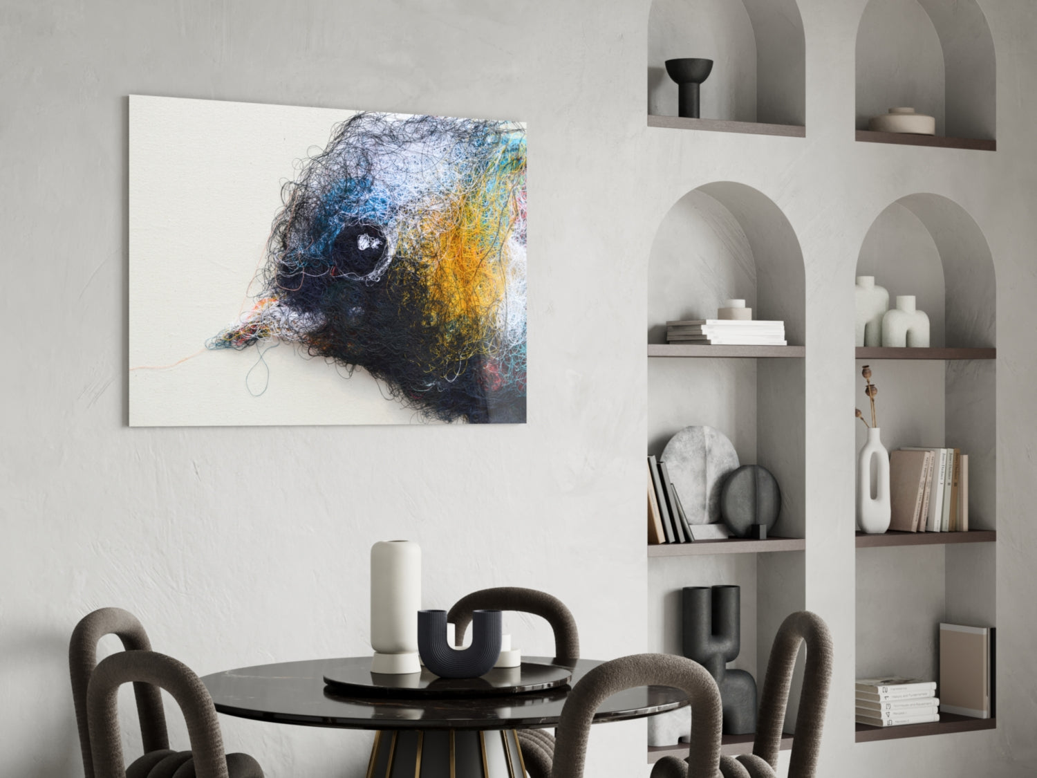 Modern dining room interior with colorful abstract bird head glass art hanging above round black table with gray chairs and white shelving unit.