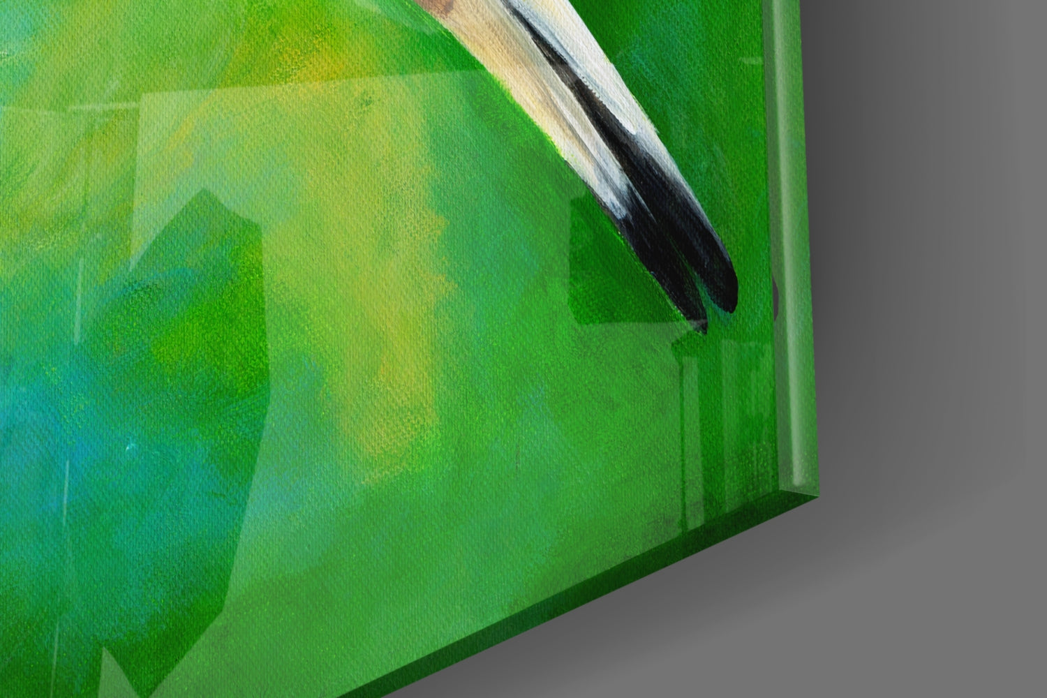 Close-up angled view of glass wall art showing a paintbrush with white handle and black bristles against layered green and yellow watercolor background.