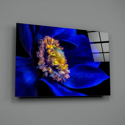 Glass wall art displaying a vibrant blue flower with yellow stamens mounted on gray wall, angled view.
