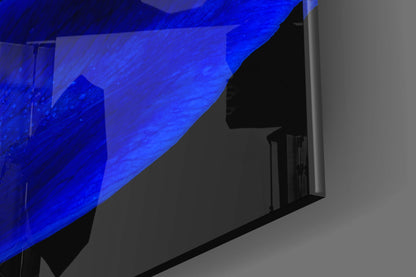 Blue illuminated glass wall art panel mounted on grey wall, photographed at angled perspective showing depth and lighting effect.