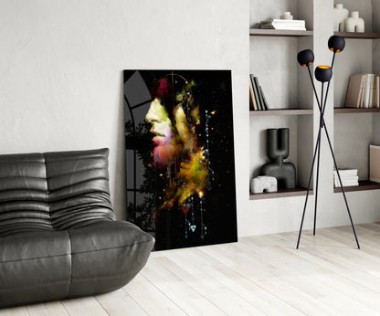 Modern living room displaying vertical glass wall art featuring a colorful abstract portrait with gold, pink, and yellow tones on black background, leaning against white wall beside gray sofa and black floor lamp.