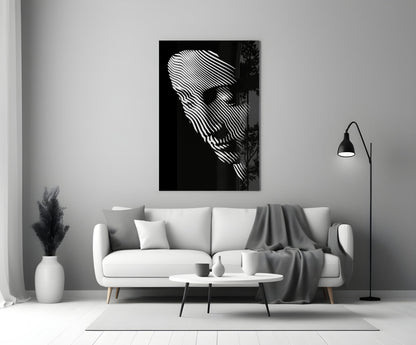 Black and white glass wall art featuring abstract striped face portrait displayed above white sofa in minimalist living room setting.