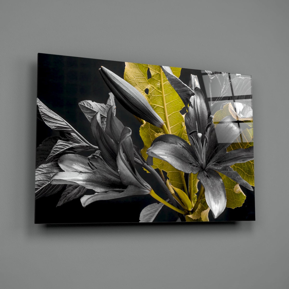 Black glass wall art displaying white lilies with vibrant yellow-green leaves against dark background, angled perspective view.