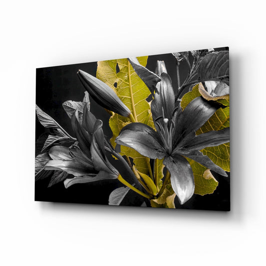 Angled perspective of black glass wall art featuring monochromatic lilies with vibrant yellow-green leaves against dark background.