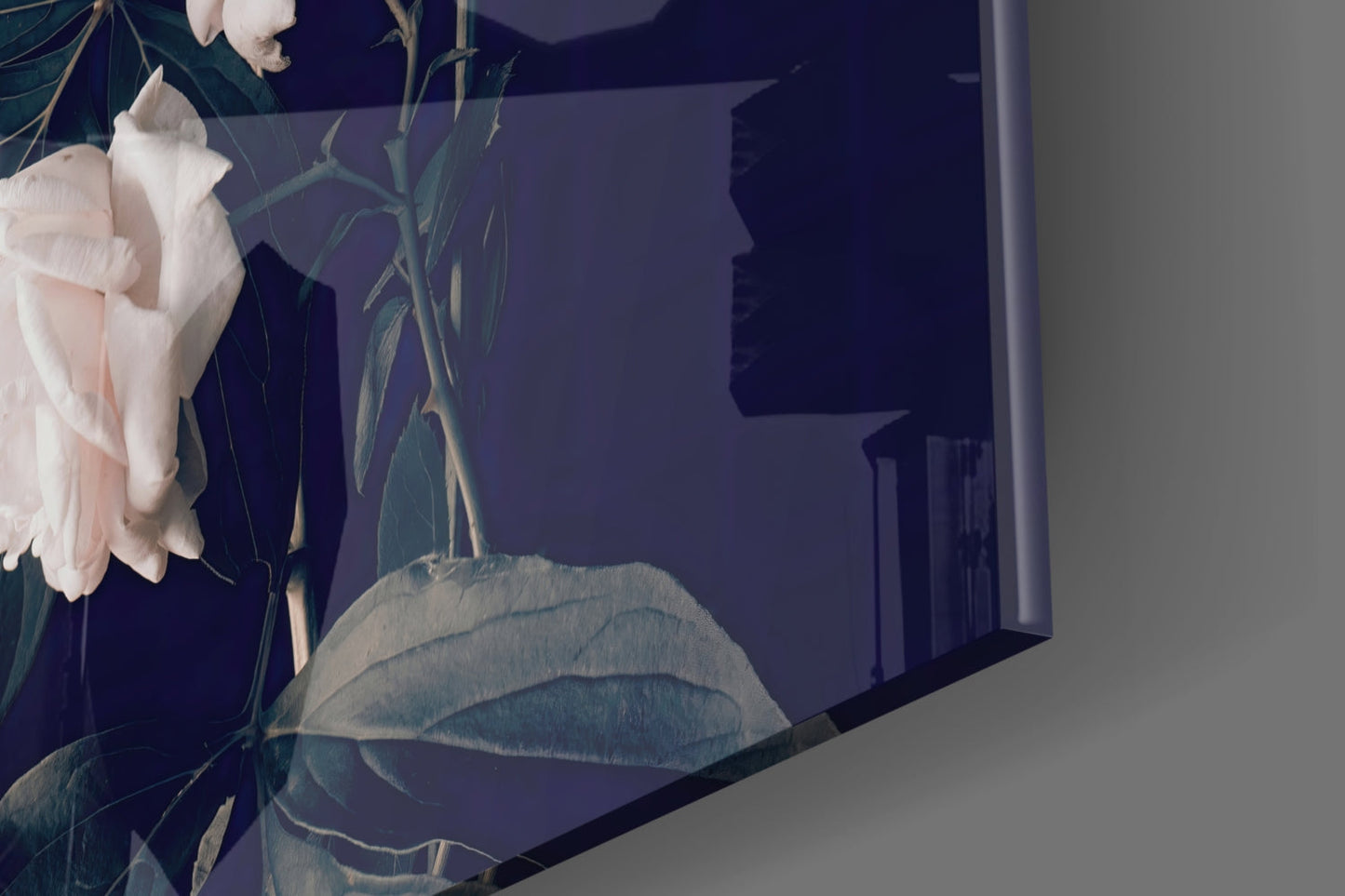 Close-up angled view of white rose glass wall art with navy blue background and botanical leaf details, mounted on light wall.