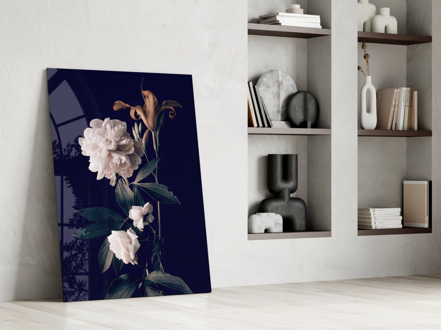 White rose glass wall art leaning against white wall beside built-in shelving with decorative objects and books.