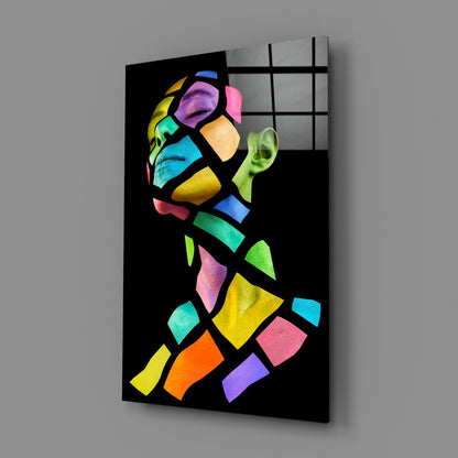Angled view of colorful glass wall art featuring a vibrant geometric portrait with neon segments against black background on gray wall.