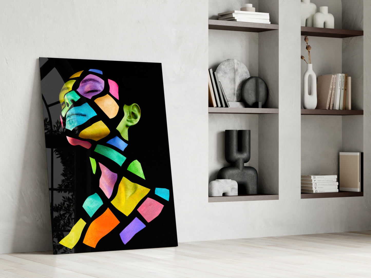 Colorful abstract portrait glass art leaning against white wall beside built-in shelving with decorative objects.