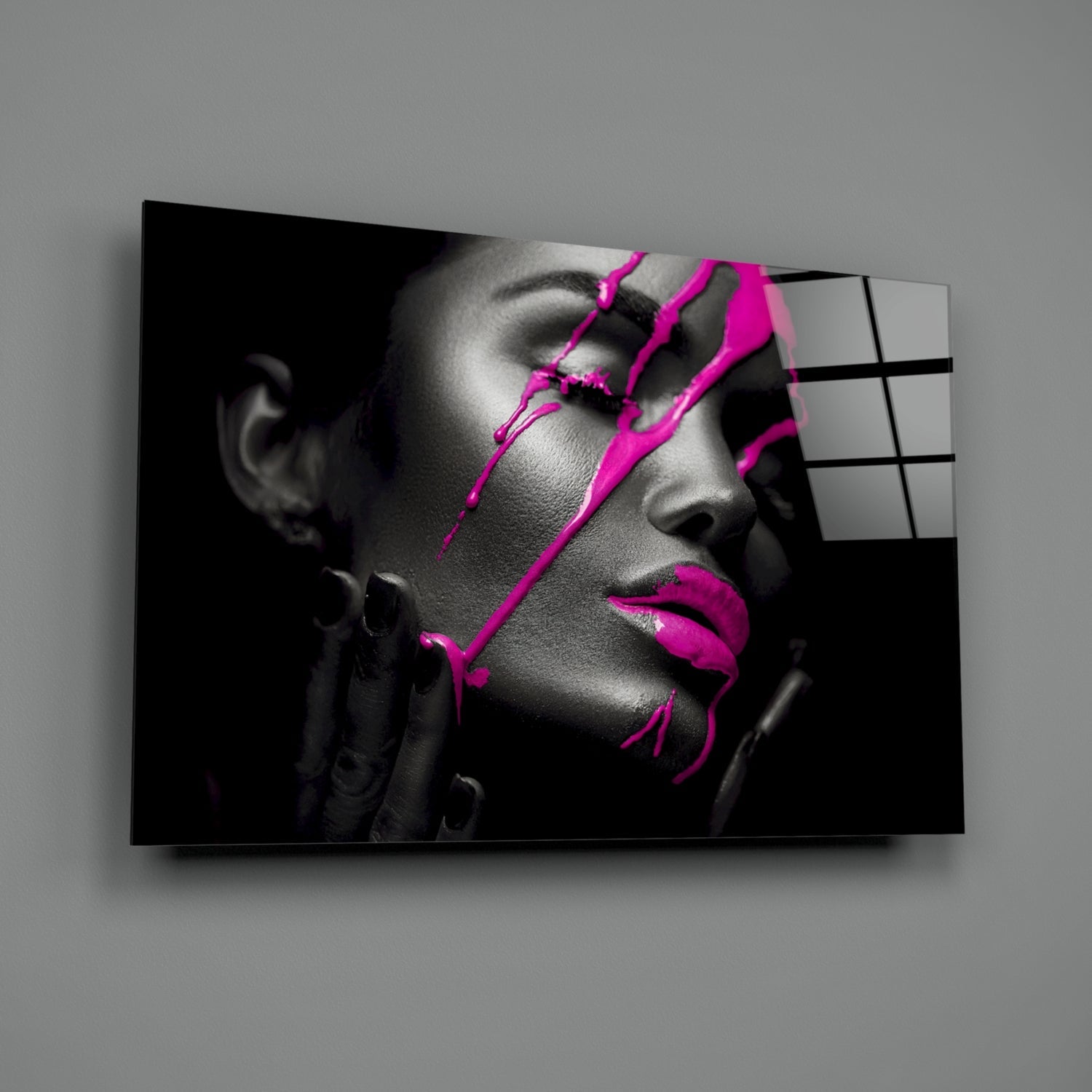 Black and white portrait of a woman with vibrant magenta paint strokes across her face, displayed on glass wall art mounted at an angle.